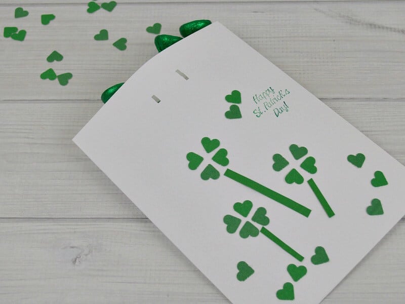 decorated white gift bag with green clovers and candy spilling out onto table