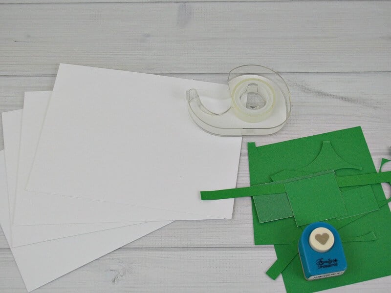 pile of white and green paper, roll of tape and heart-shaped paper punch on white table