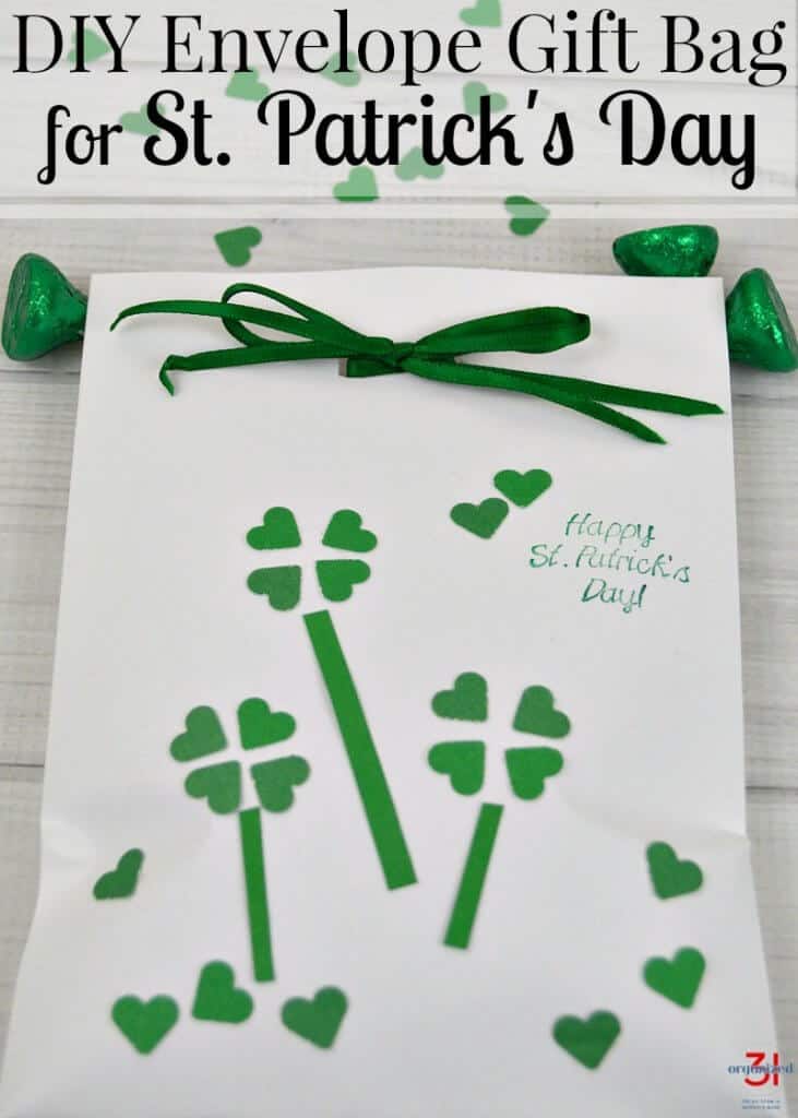 overhead view of white bag with green bow and 4 leaf clover decorations on table with green candy and green hearts scattered on table with title text reading DIY Envelope Gift Bag for St. Patrick's Day