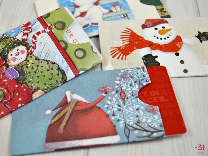 close up of 4 Christmas-themed gift card sleeves on white wood table.