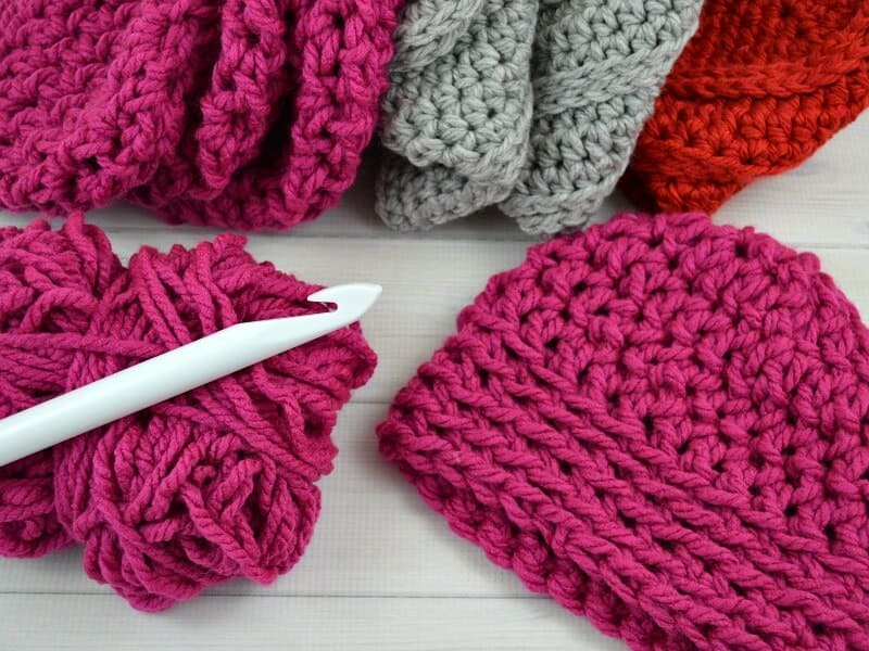 pile of crocheted hats with yarn and crochet hook