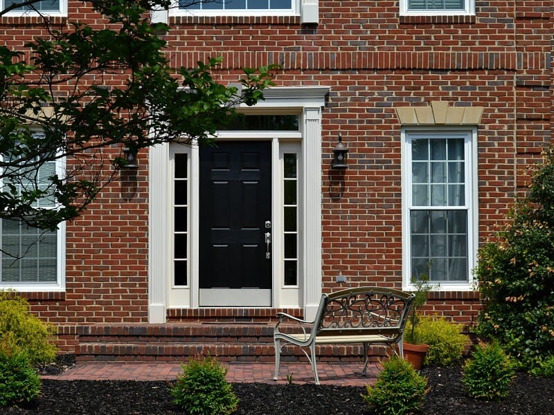 black front door in a red brick house with green bushes  landscaped