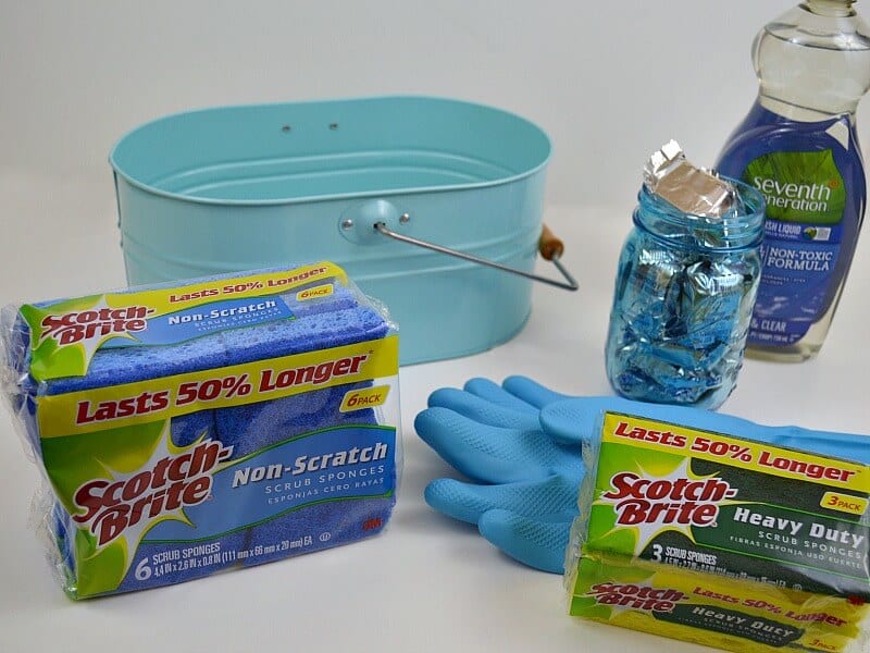 empty blue caddy, packages of blue sponges, container of liquid dish soap and jar of dish washer tabs on white table