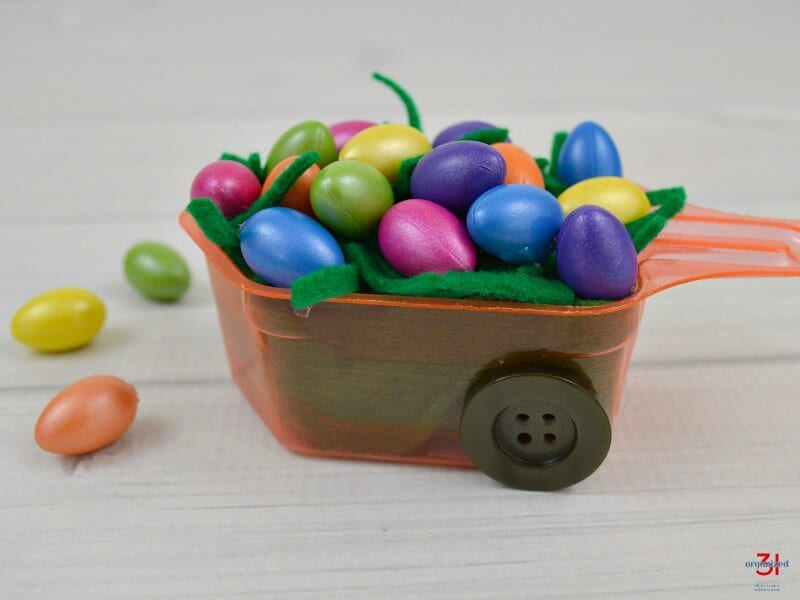 orange DIY wheelbarrow holding colorful Easter eggs on white wood table