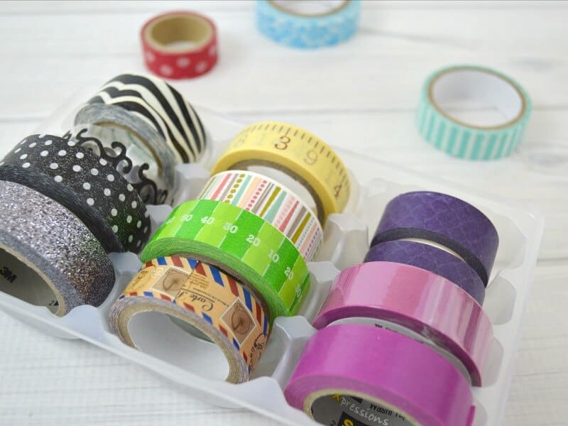overhead view of rolls of brightly colored washi tape in organizing tray on white table