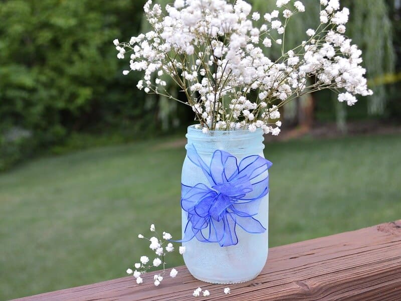 close up of light blue jar with blue bow and white baby's breath on a  piece of wood outside