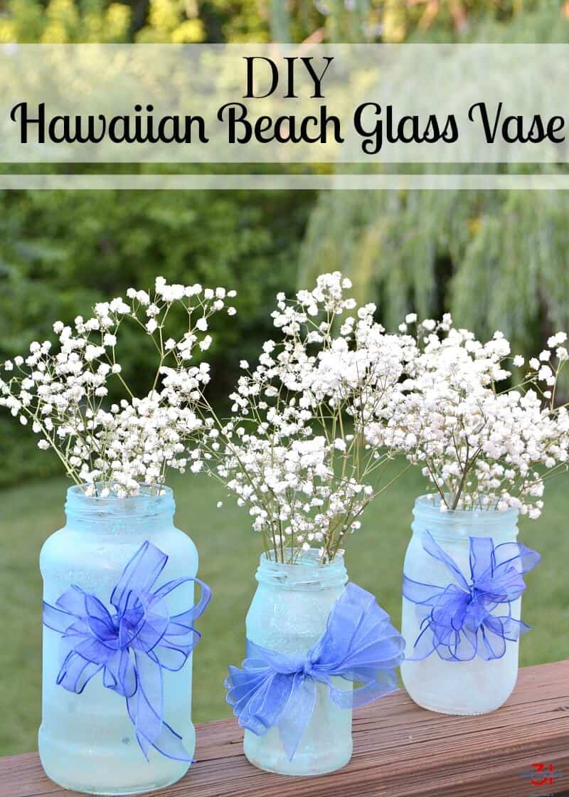 3 light blue jars holding white flowers and blue bows on table outside with title text reading DIY Hawaiian Beach Glass Vase