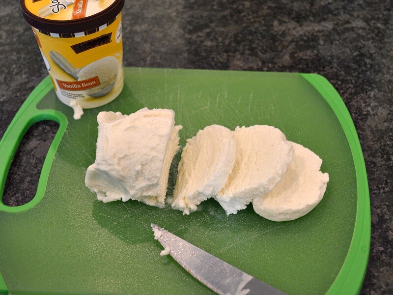 small carton of ice cream with ice cream on cutting board cut into round slices
