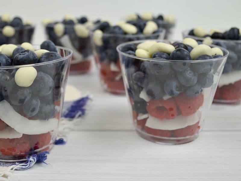 side view of clear cups of red, white and blue fruit on white wood table
