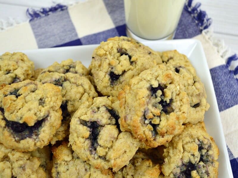 overhead close up of blueberry cookies white plate sitting on blue and white tablecloth and glass of milk