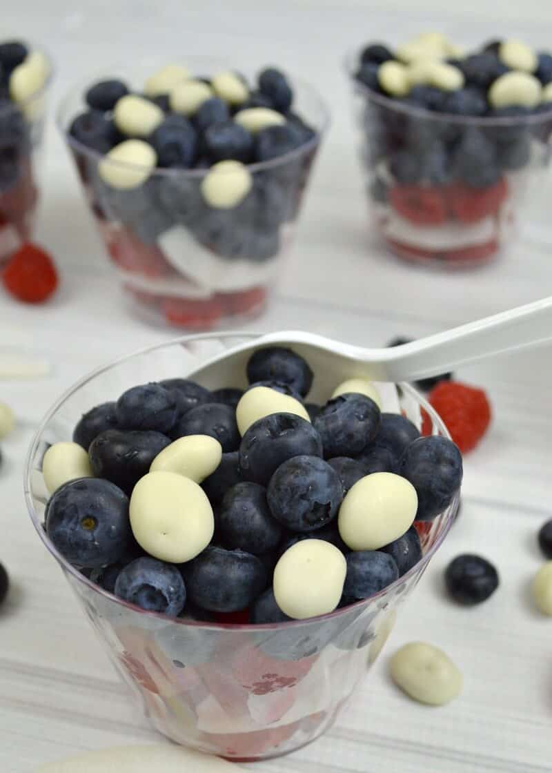 close up of bowl of red, white and blue berries with more bowls on table and scattered fruit