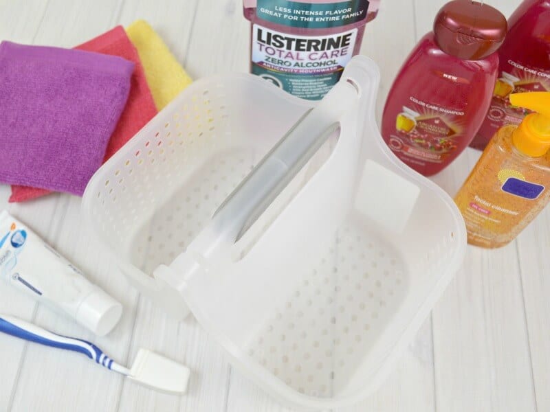 overhead view of empty shower caddy with personal care items and stack of washcloths next to it