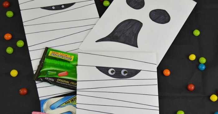 3 decorated envelopes to look like a mummy and ghost with candy scattered on black background