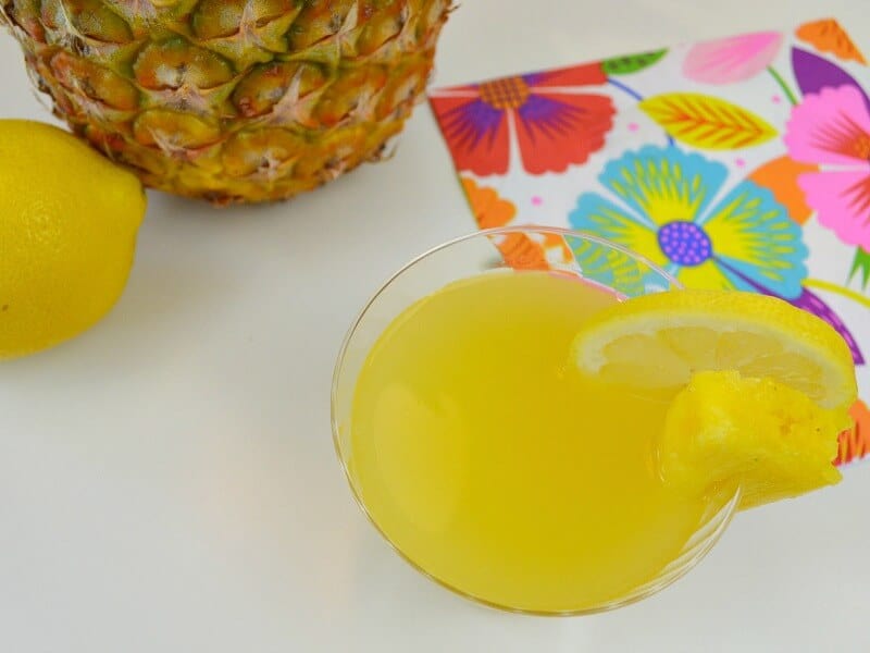 overhead view of yellow drink and pineapple and lemon on table with floral napkins.