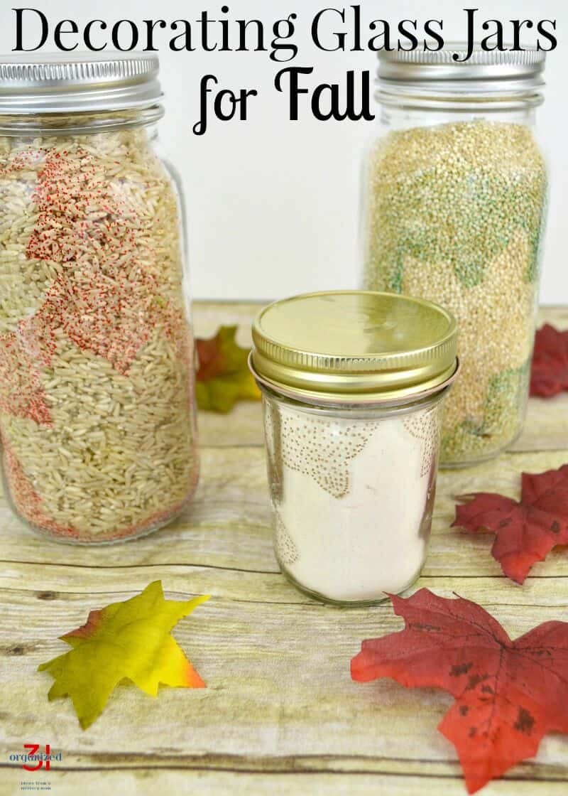 3 jars filled with rice and flour and decorated with leaf motifs on wood table with autumn leaves with title text reading Decorating Glass Jars for Fall