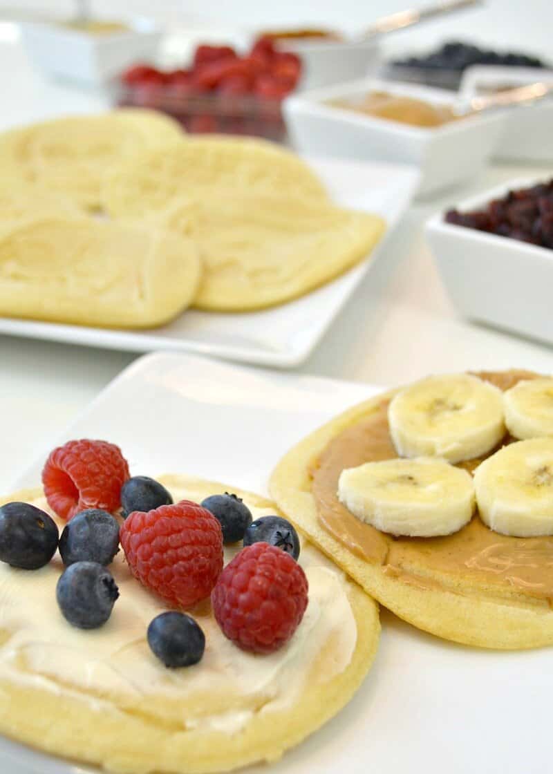 two waffles with spreads and fruit on white plate in foreground and ingredients in the background