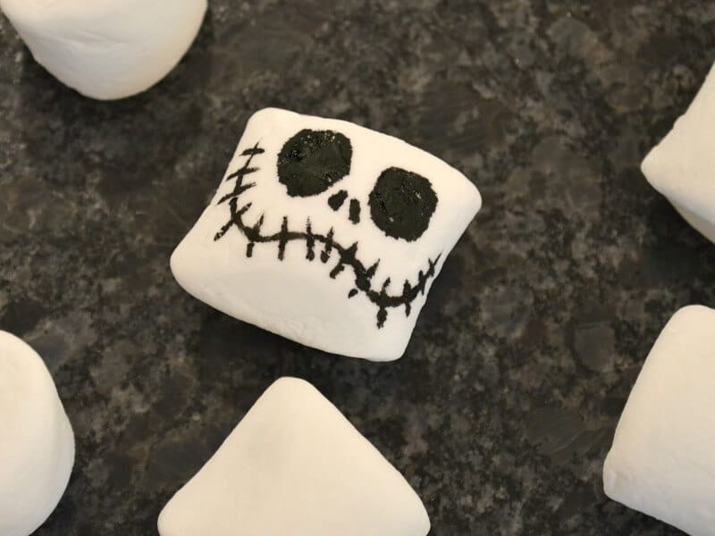 close up of one marshmallow with skeleton face with blank marshmallows on black counter