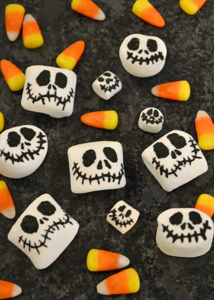 Overhead view of 10 smiling skeleton faces on marshmallows with candy corn scattered