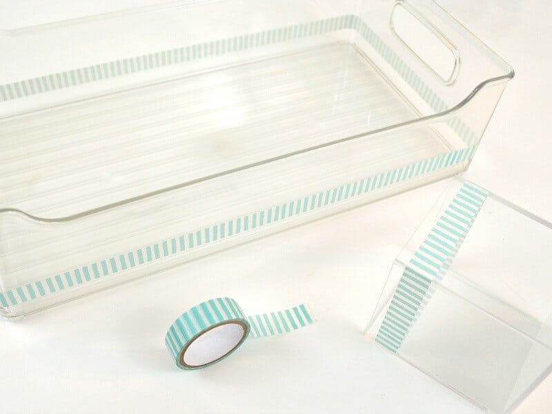 2 clear organizing bins with blue and white washi tape on the top edge and roll of washi tape on table