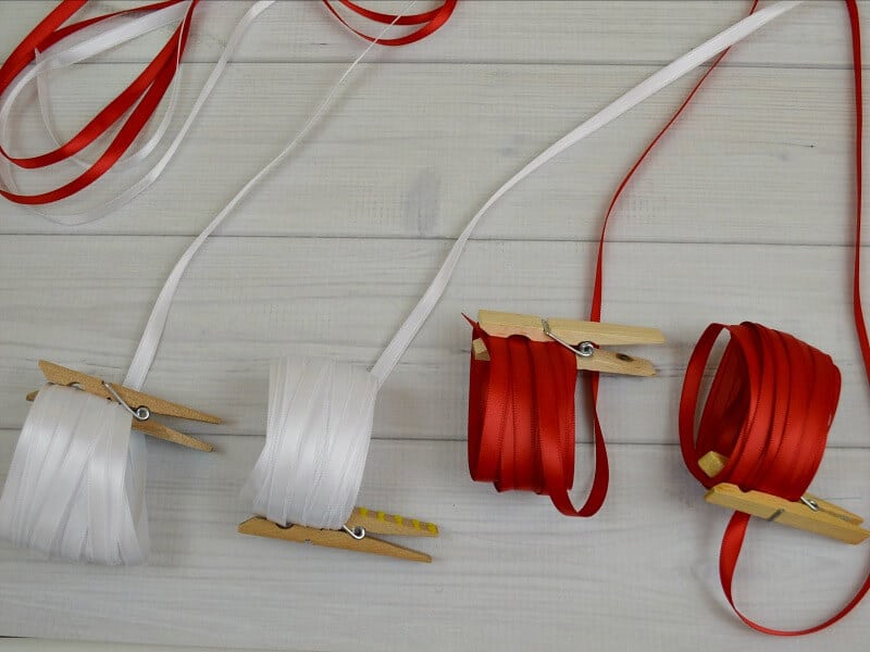 4 rolls of ribbon, two red and two white, clipped with wood clothes pins.