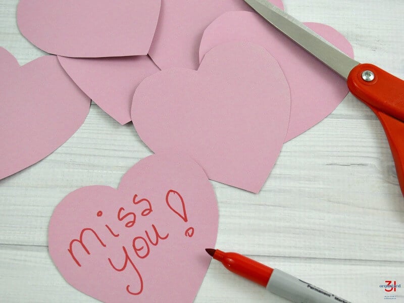 pink paper hearts with red marker and red scissors and note saying "miss you".