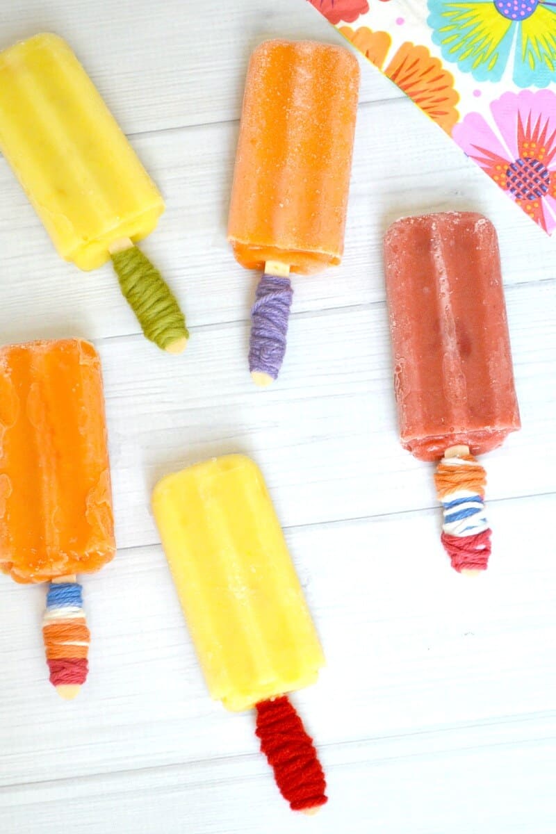 Overhead view of 5 popsicles with holders and a colorful napkin nearby