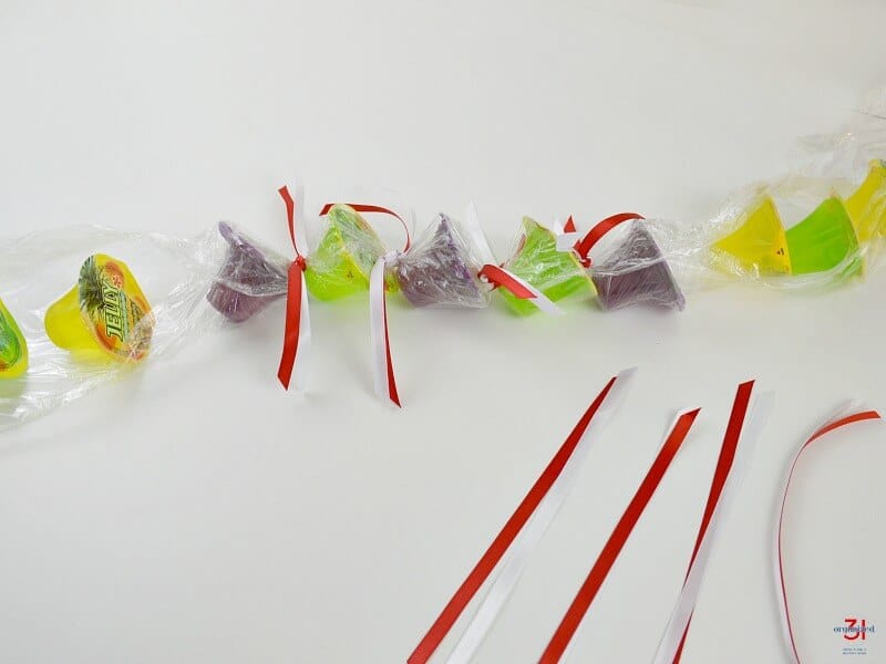 candy in clear cellophane with red and white ribbons tied between some candy and other ribbons laying on table