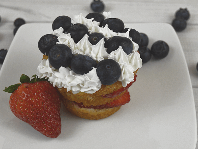 strawberry shortcake with rows of blueberries and white icing on white plate with strawberry and blueberries scattered around