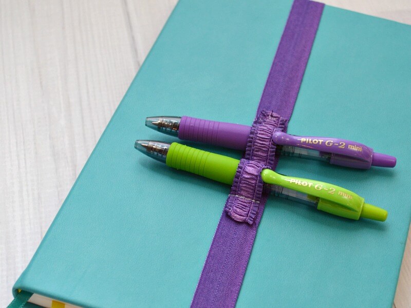 close up of purple strap holding 2 pens on blue journal 