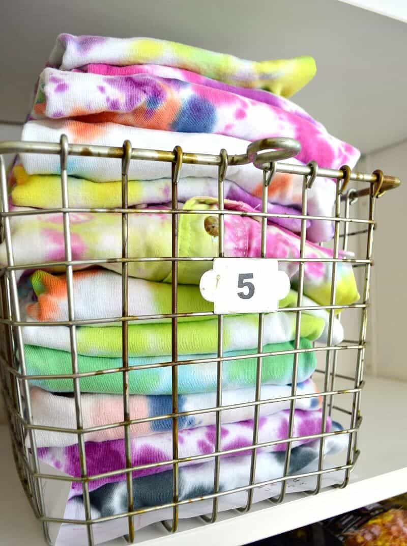 Neatly folded tie dye fabric stacked in wire locker basket.