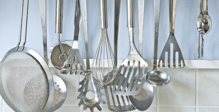 Metal kitchen utensils hanging in front of blue and white tile wall