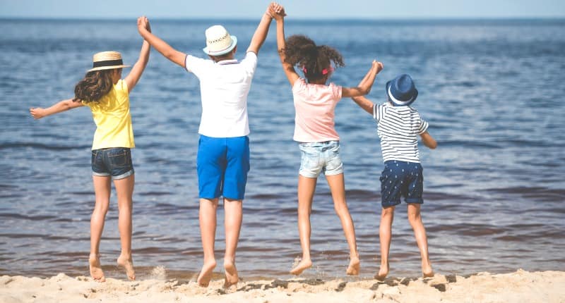 4 children holding hands and jumplng at the beach