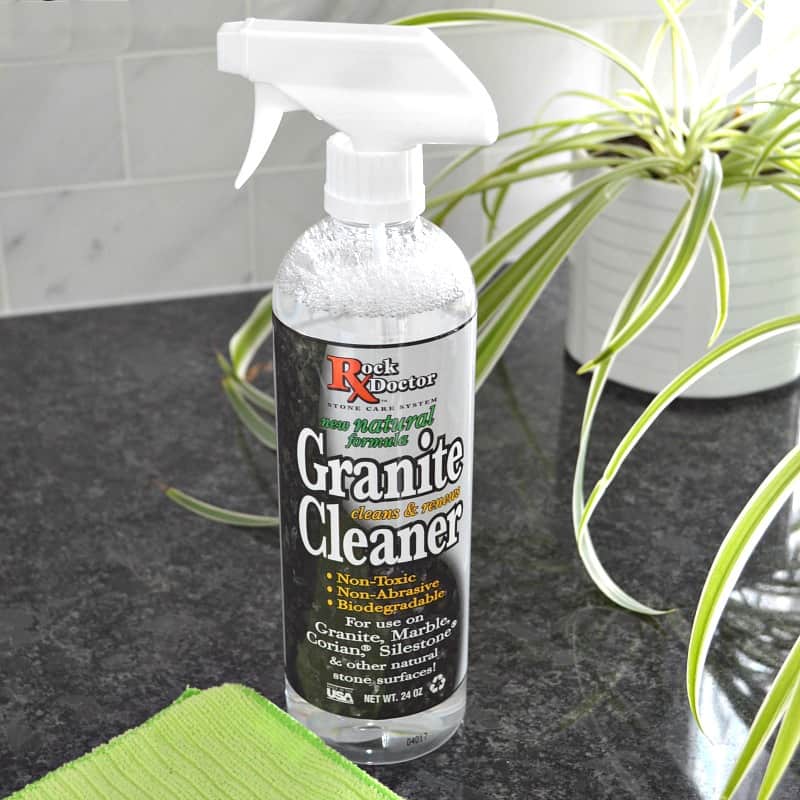 spray bottle of granite cleaner on black countertop with green plant in white pot