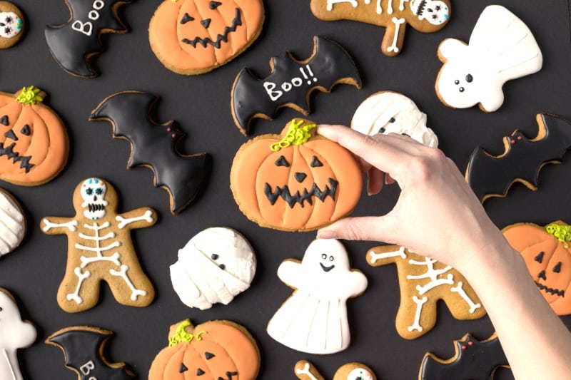 Hand reaching for jack o'lantern cookie from many Halloween cookies