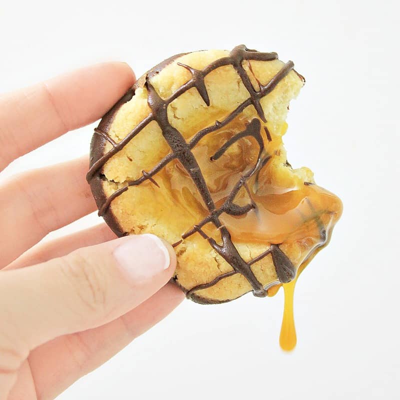Hand holding a twix cookie with bite taken out and caramel dripping