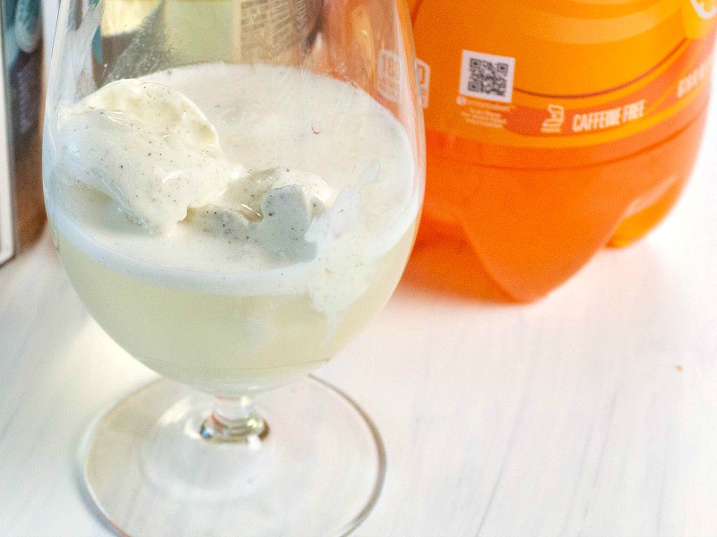 close up of scoop of vanilla ice cream in frothy liquid in a glass with an orange soda bottle in the background