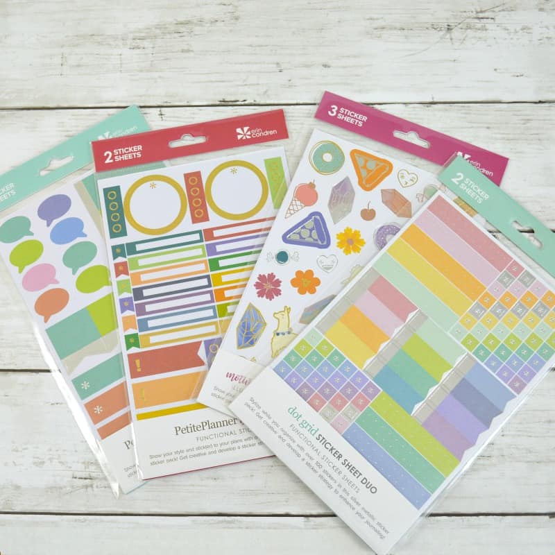 4 packs of colorful Erin Condren planner stickers on white wood table.