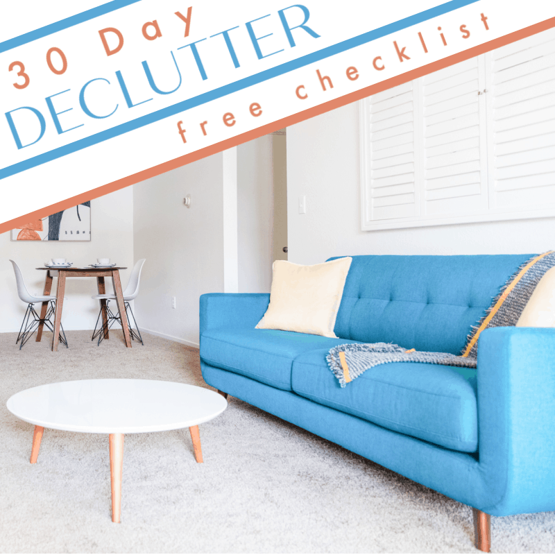 neatly organized living room blue couch & white round table with title text reading 30 Day Declutter free checklist