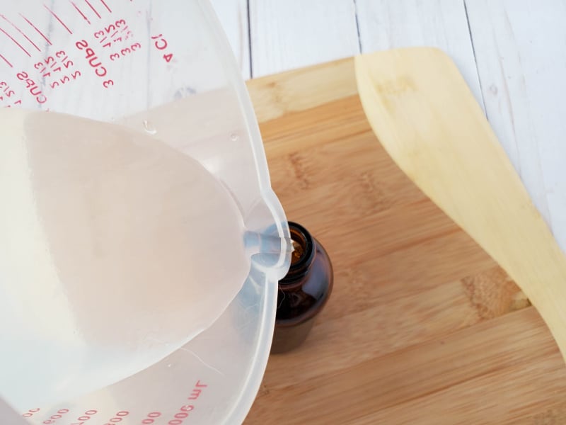 large plastic bowl pouring liquid into small brown bottle on wood cutting board