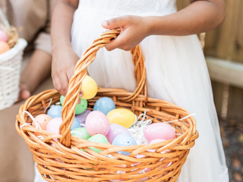 girl in white dress holding basket of colorful plastic eggs