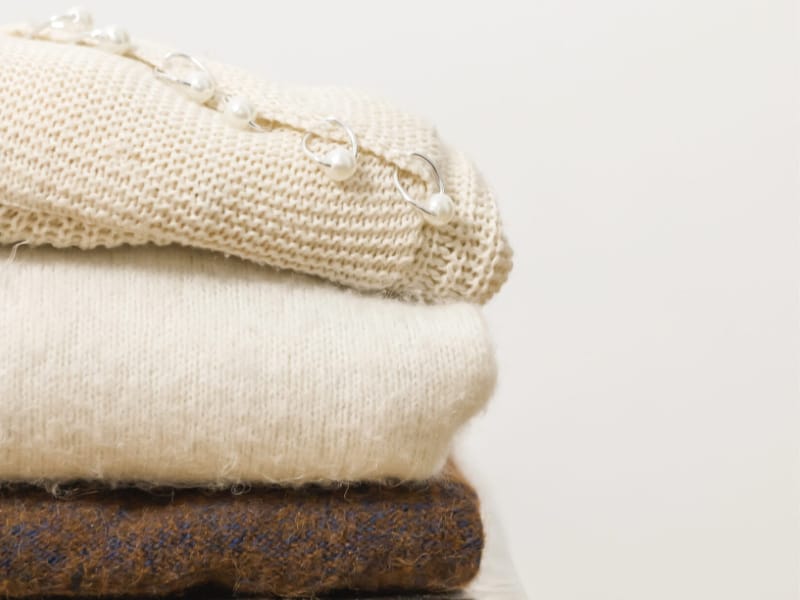stack of 3 folded sweaters in cream and brown.