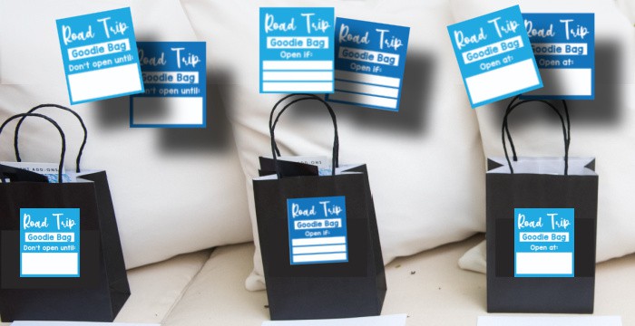 3 black bags with labels on them reading Road trip Goodie Bag with several other labels above them on pillows