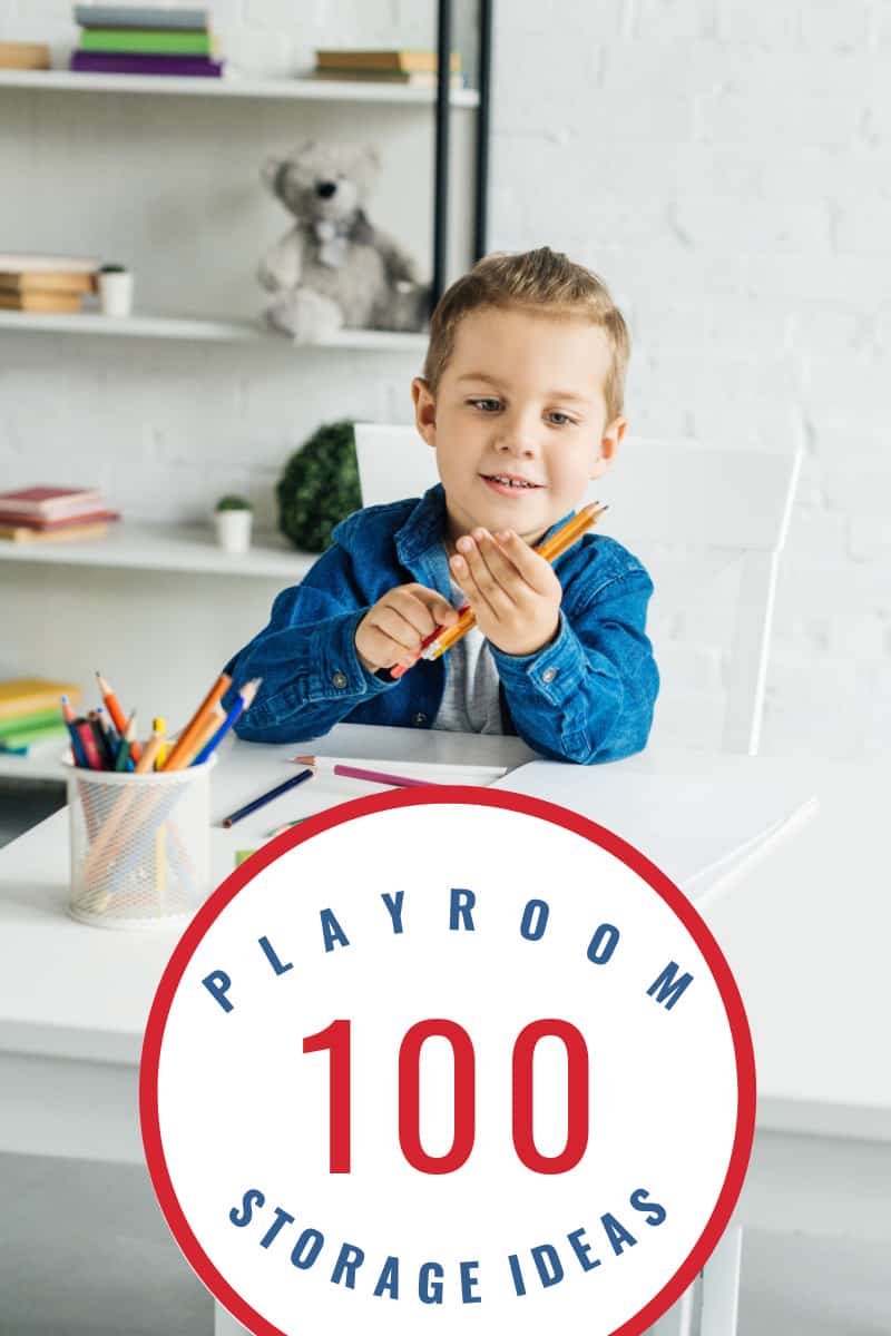 boy in blue shirt holding pencils at table in playroom
