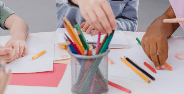 child's hand reaching for colored pencil in cup.
