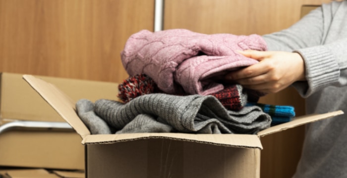hands placing folded clothes in brown box
