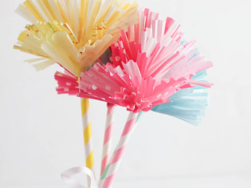 yellow, pink and blue paper flowers on striped stem with white ribbon tying them together