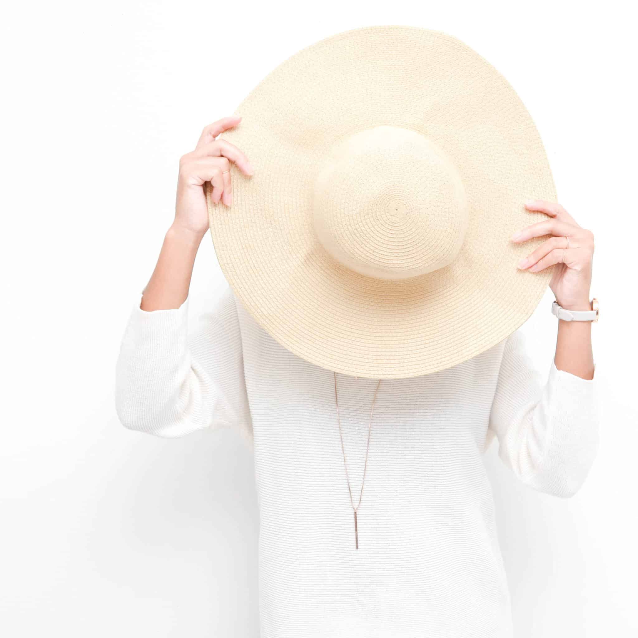 woman holding light colored sun hat in front of her face