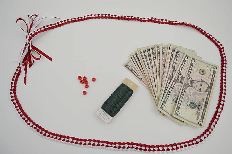 red and white ribbon lei with red beads, spool of floral wire and stack of $5 bills fanned out on white table