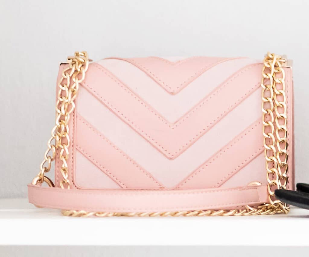pink and white purse with chain strap on white shelf.