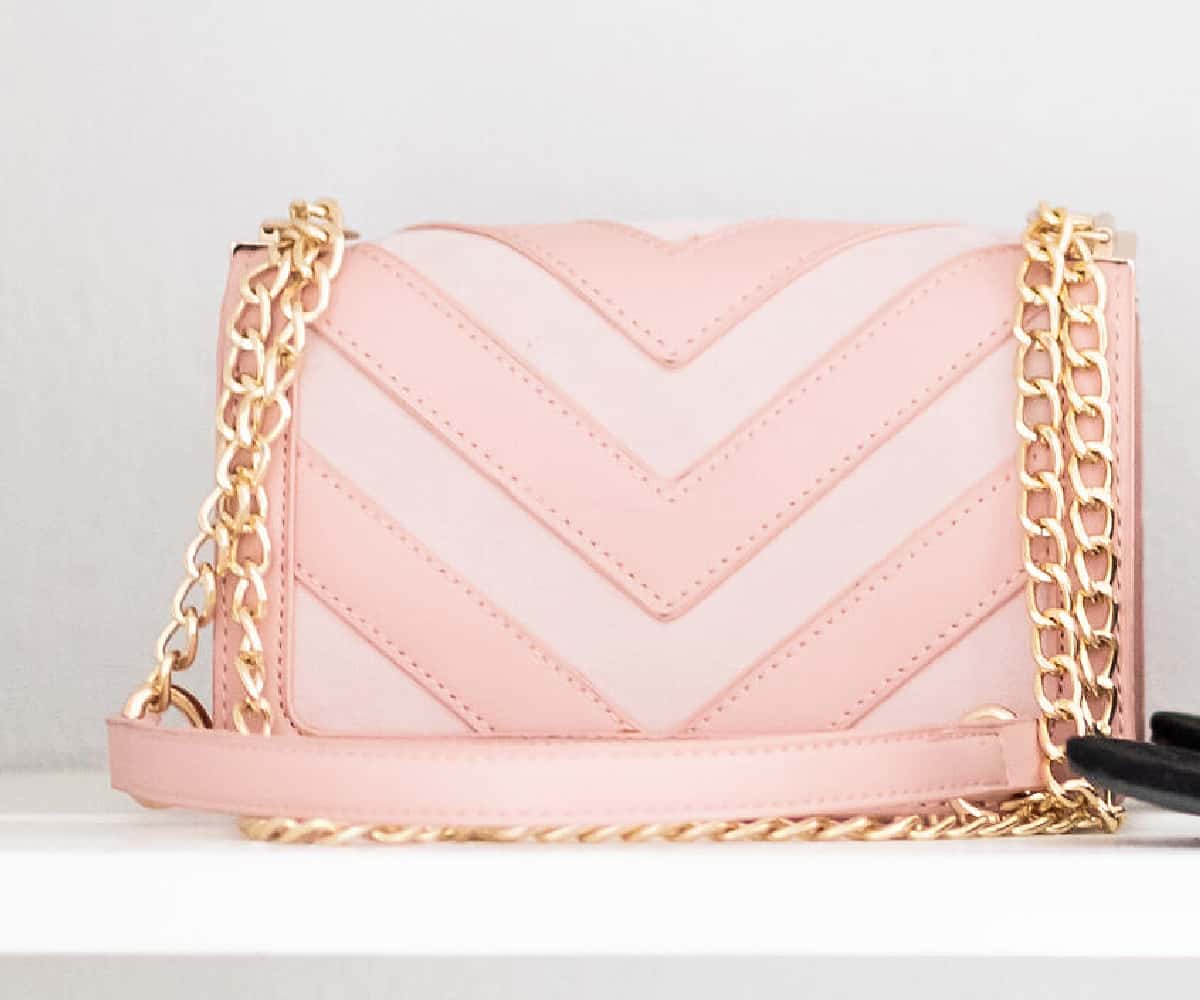 pink and white purse with chain strap on white shelf